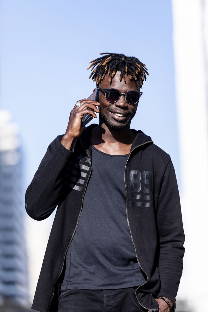 Black smiling man with sunglasses using mobile phone outdoors