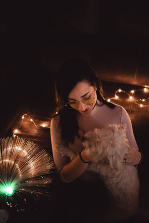 Young woman with dog between fairy lights in darkness