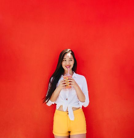 Beautiful woman having a refreshing smoothie against a red wall