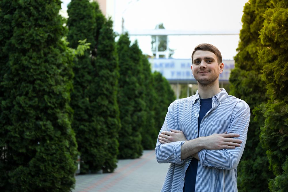 Young man in shirt with folded hands against university. Study