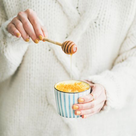 Woman in sweater adding raw honey to latte cup