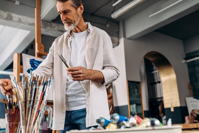 Man with grey beard going through his brushes in an art studio