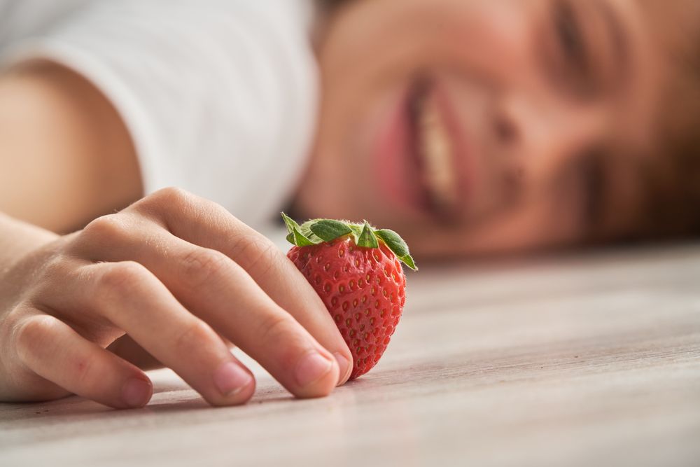 Crop kid lying on floor with strawberry