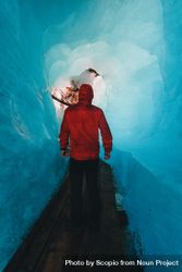 Back view of person in red jacket walking in an frozen cave 56drdb