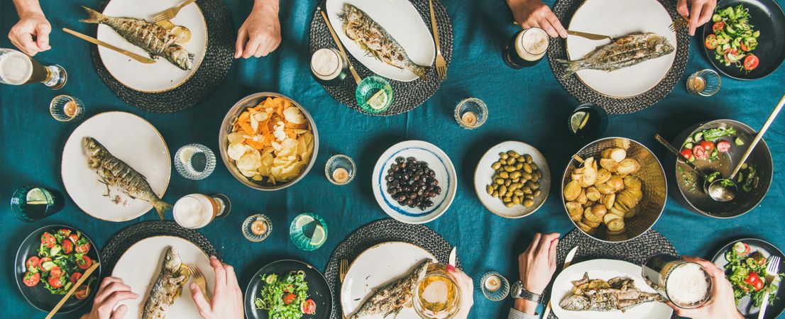 Flat-lay of human hands, beer glasses, grilled sea bass