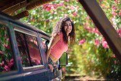 Happy female in pink t-shirt leaning out of car window