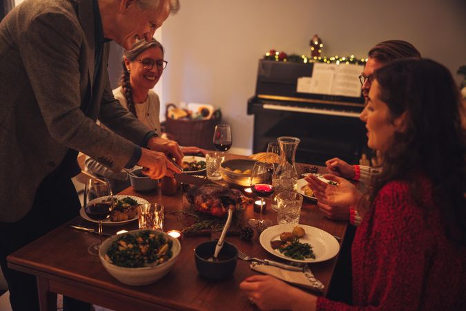 Older man serving traditional stuffed roasted turkey to family sitting at dinner table