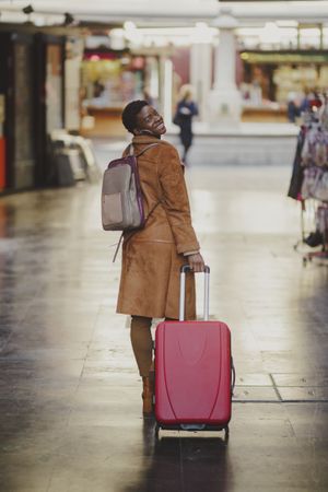Stylish Black woman with luggage walking on street
