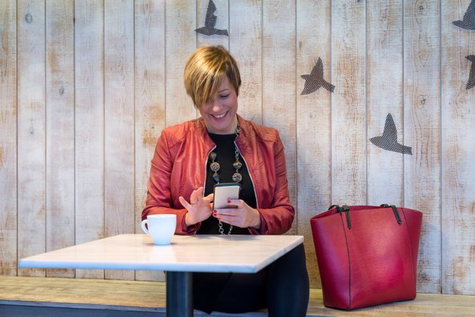 Female in red coat sitting in cafe smiling while texting