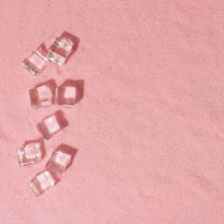Flat lay of ice cubes on pink sand background with shadows