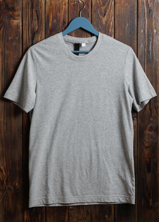 Hanger with blank gray t-shirt on wooden background, space for text
