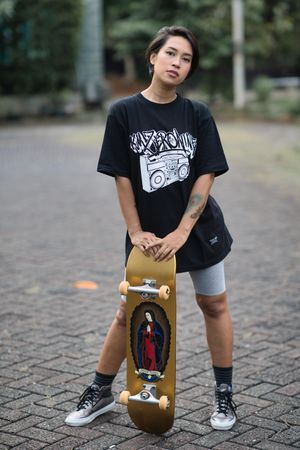Woman in dark shirt holding skateboard standing outdoor