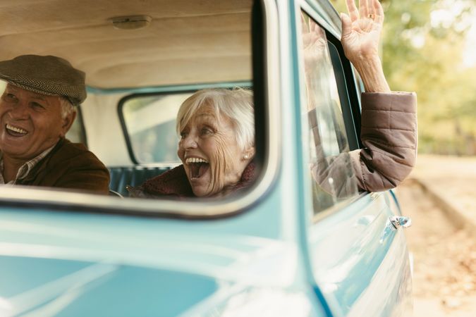 Excited woman raising her hand out of the car and laughing with her husband