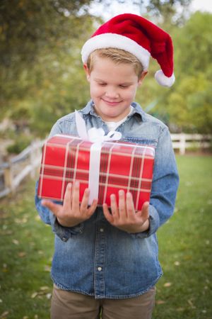 Young Boy Wearing Santa Hat Holding Christmas Gift Outside