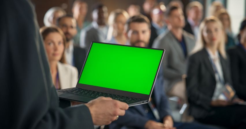 Back View, Focus on Hands Of Startup CEO Holding Laptop With Green Screen Chromakey On Display And Pitching Product Or Service to Room Full of Investors.