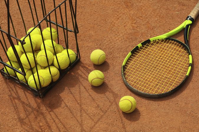 Racket and basket with tennis balls on clay court