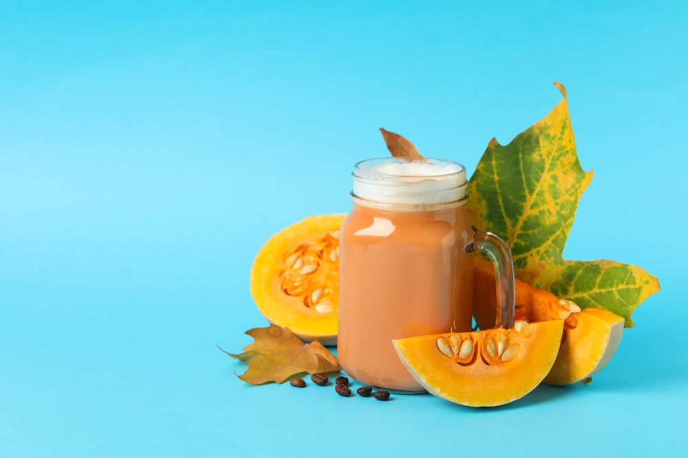 Composition with glass jar of pumpkin latte on blue background