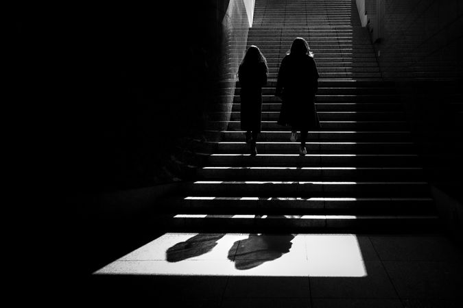 Silhouette of two people climbing stairs in grayscale