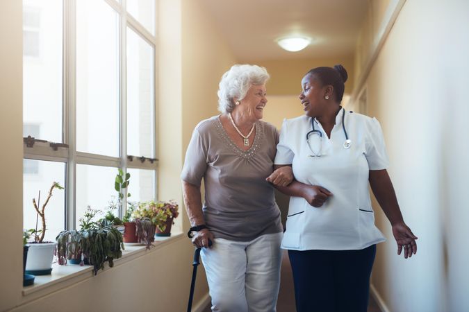 Portrait of smiling healthcare worker walking and talking with older woman
