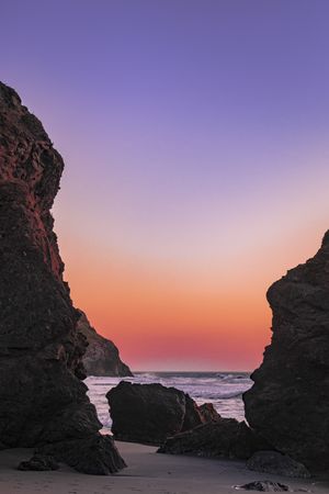 Sunset over Pacific Ocean seen from rocky beach, vertical