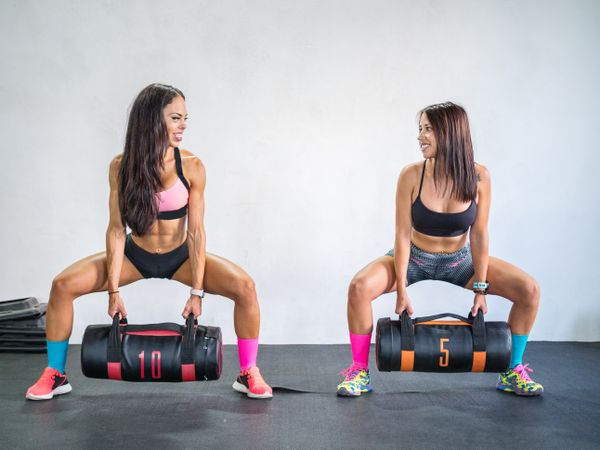 Happy sportswomen training with sand bags in modern gym