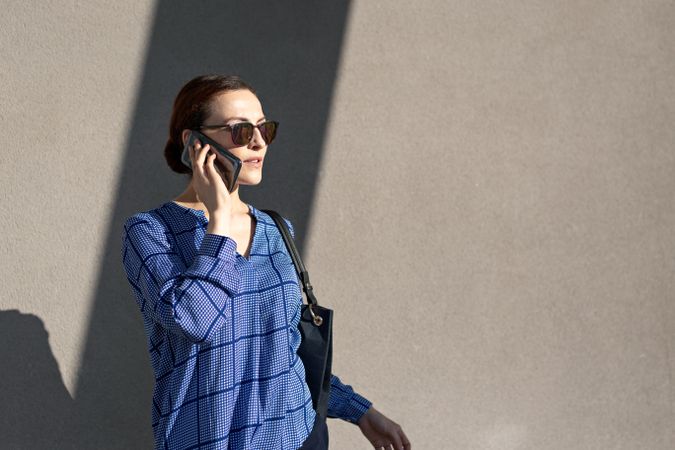 Businesswoman having smartphone conversation near gray wall