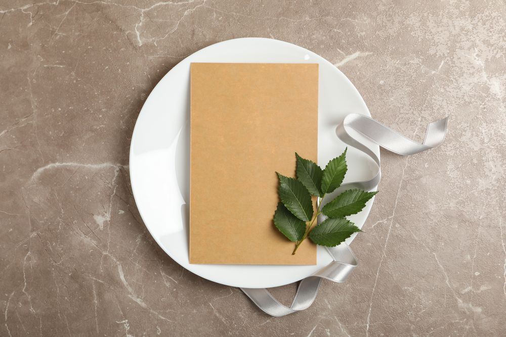 Plate with blank cardboard sheet, leaf and ribbon on gray background