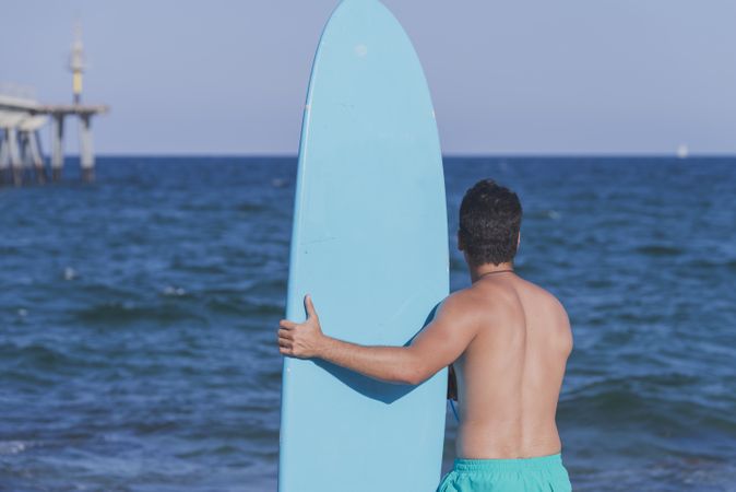Male surfer holding his surfboard looking out to the ocean