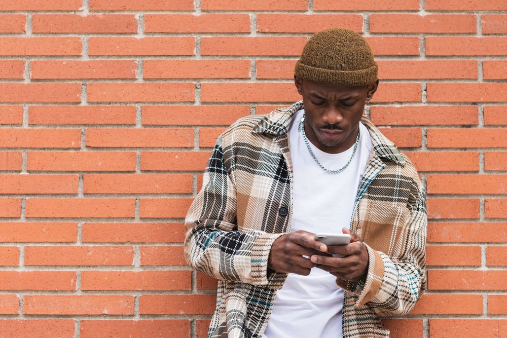 Black man using smartphone near brick wall