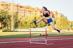An athletic woman jumping hurdles on an athletics track.
