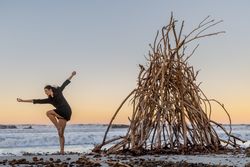 Young woman dancing on shore near water and wooden twigs placed for campfire