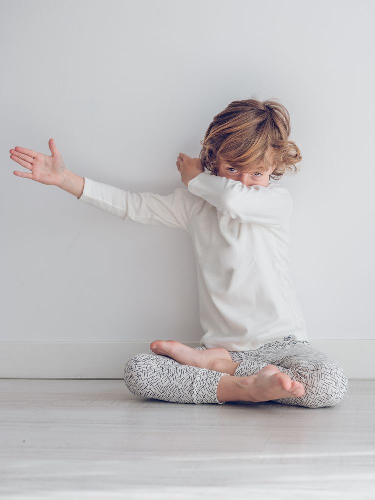 Boy in white pajamas leaning against the white wall of his house.