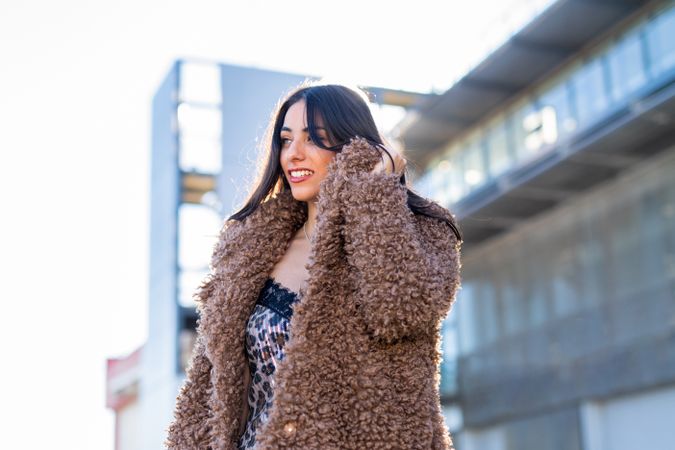 Cheerful woman wrapping in coat on street