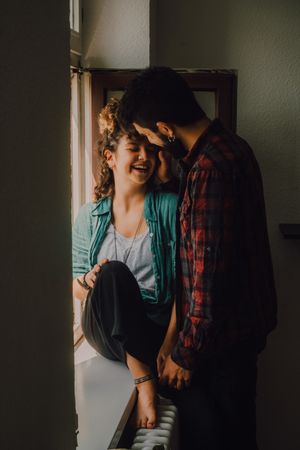 Happy couple embracing on window sill at home