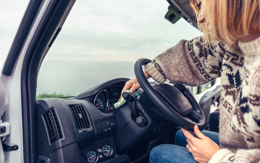Female in warm sweater cleaning dashboard of parked vehicle, vertical
