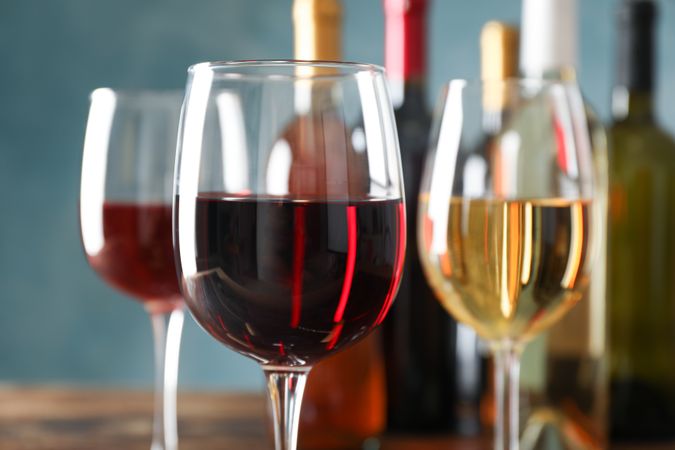 Glasses and bottles with wine on wooden table, close up