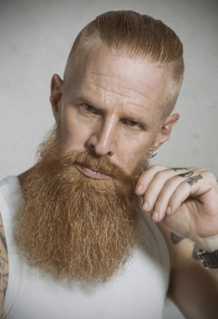 Confident adult red haired hipster tightening mustache and looking at camera