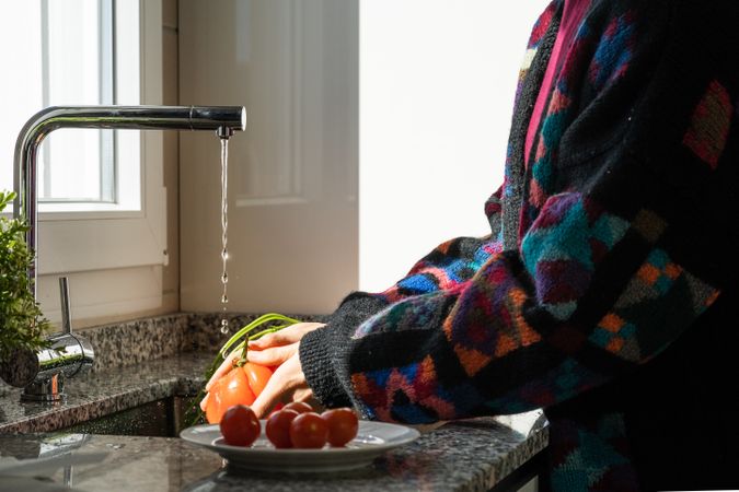 Crop woman washing tomato over sink