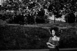 B&W shot of contemplative woman in dress standing in park looking in the distance