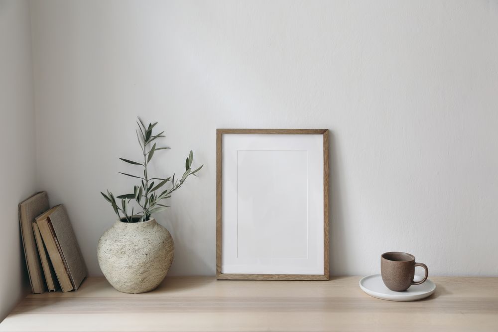 Wooden table with vase of eucalyptus branches, books and mug with mockup poster