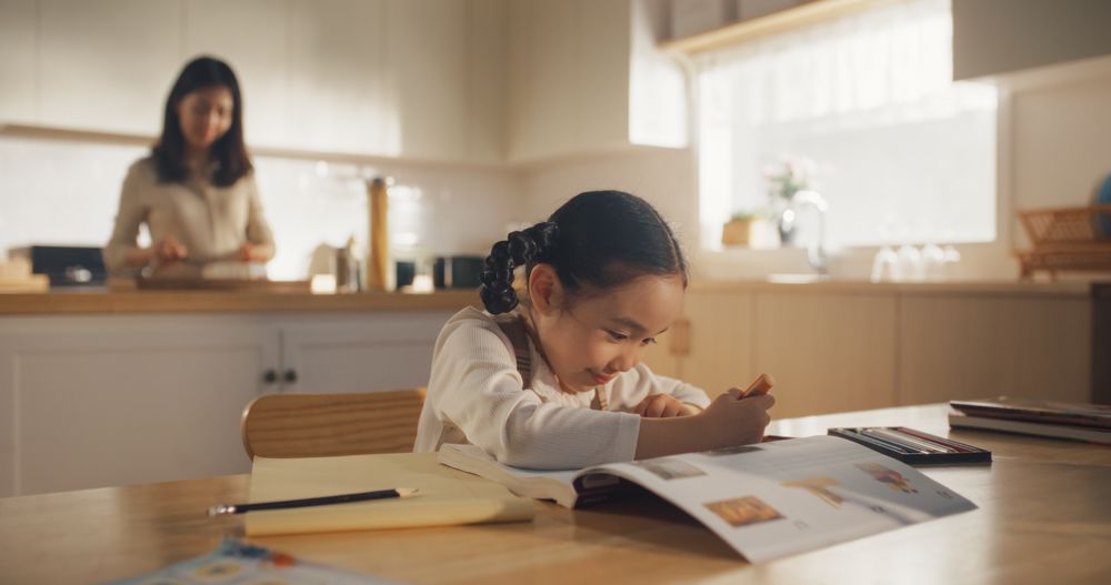 Portrait of a Little Korean Girl Sitting at a Kitchen Table at Home, Doing her Homework in the Morning