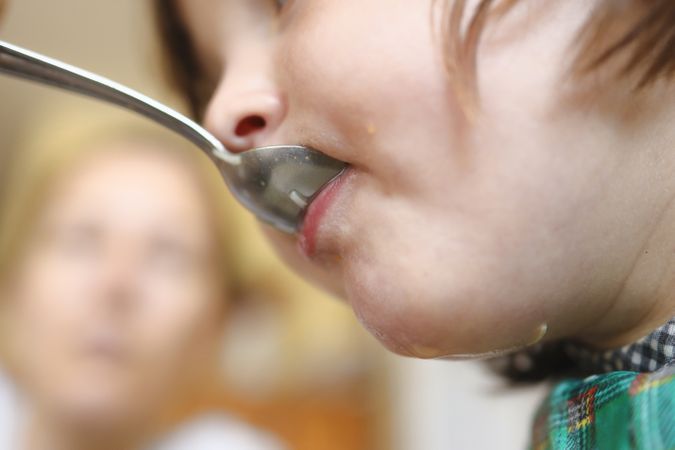 A kid eating soup with the help of her mother.