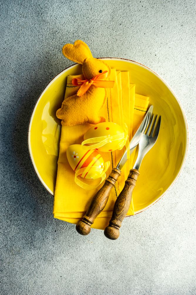 Top view of Easter table setting with yellow plate and Easter ornaments