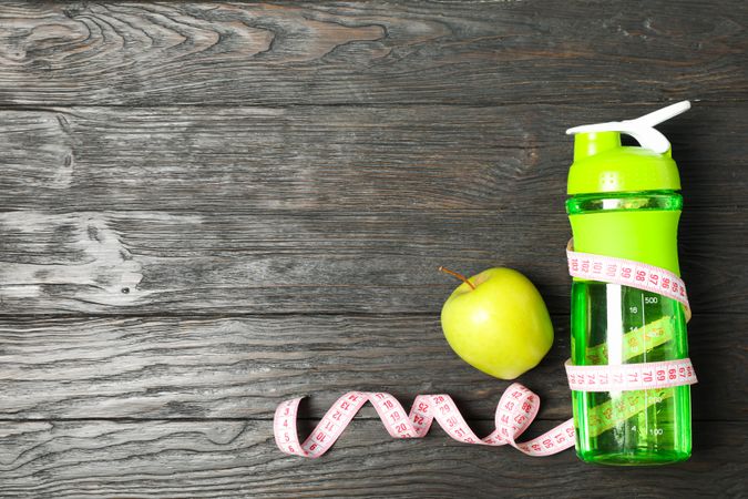 Bottle, measuring tape and apple on wooden background, copy space