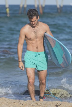 Front of male surfer with blue board in front of the shore