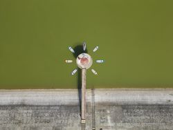 Aerial view of a multiple surfboards forming a flower around a concrete object on the lake with two women resting in the sun