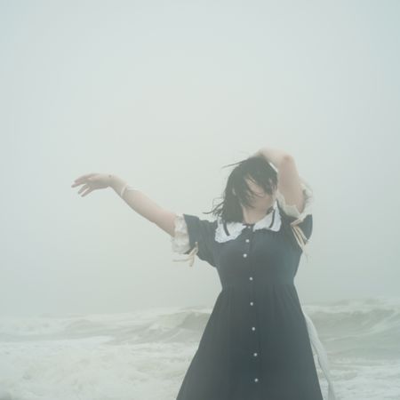 Woman in dark dress raising arms and standing on seashore