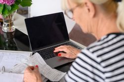 Mature woman watching bills and mail bank notice, sitting at living room table at home