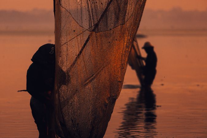 Silhouette of two people holding fish net during sunset