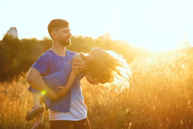 Man playfully carrying daughter through meadow
